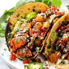 two tacos on a white plate with lettuce, tomatoes and other toppings