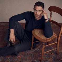 a man sitting on top of a wooden chair next to a rug and holding his hand near his face