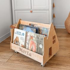 a wooden toy house with books in it on the floor next to a basket full of children's books