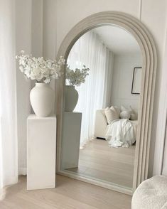 a white vase with flowers sitting on top of a table next to a large mirror