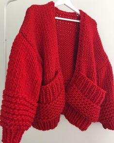 a red cardigan sweater hanging on a hanger in front of a white wall