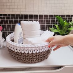 a person is holding a basket with towels and toothpaste on it in front of a tiled wall