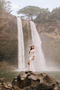 a woman standing on rocks in front of a waterfall