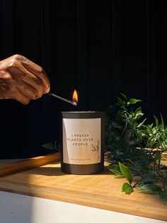 a person lighting a candle on top of a wooden table next to plants and greenery