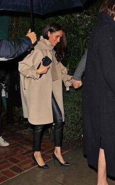 a woman in black pants and coat holding an umbrella while standing next to a man