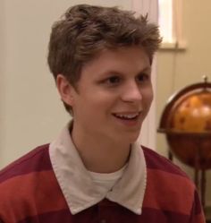 a young man wearing a red and white striped shirt smiles at the camera while standing in front of an antique globe