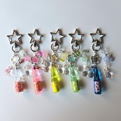 six different colored bottles with charms attached to them on a white surface and one has a star shaped keychain