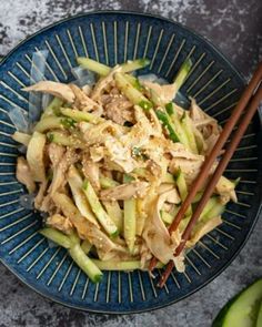 a blue bowl filled with food and chopsticks next to cucumber slices