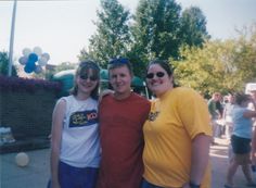 two women and a man are posing for a photo at an outdoor event with balloons in the background