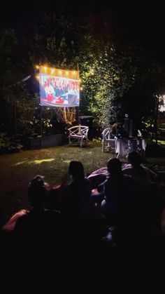 people sitting in the grass watching an outdoor movie on a big screen at night time