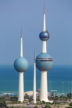 three tall buildings with blue and white domes in front of the ocean