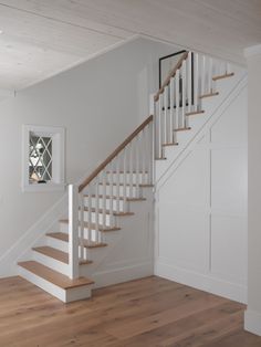 a white staircase with wooden handrails and hardwood floors in an empty room next to a window