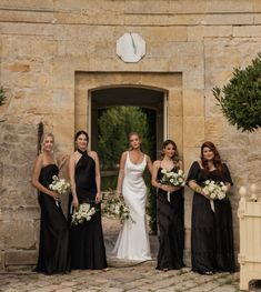 a group of women standing next to each other in front of a stone building holding bouquets