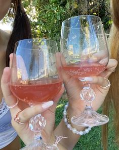 two women are holding up wine glasses in their hands while sitting on the grass outside