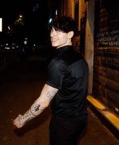 a young man with tattoos on his arm walking down the street at night in front of a building