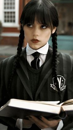 a woman with long black hair wearing a school uniform and holding an open book in her hands