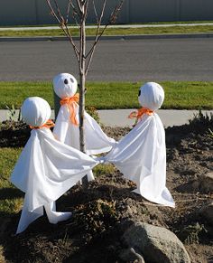 three white cloth ghost figures holding hands in front of a bare tree with no leaves