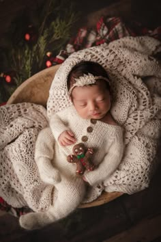 a newborn baby wearing a white sweater and holding a teddy bear in a wooden bowl