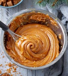 a bowl filled with peanut butter and topped with a whisk next to a spoon