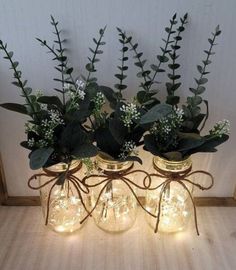 three mason jar vases with lights and greenery in them are sitting on a table