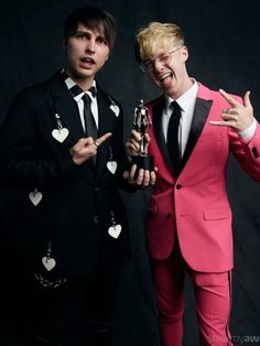 two young men in suits posing for the camera with an award and one pointing at something