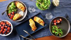 several plates with food on them sitting on a blue table cloth next to silverware and utensils