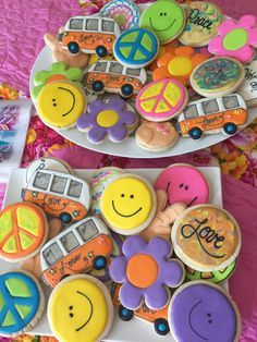 two plates filled with decorated cookies on top of a pink table cloth covered in flowers and peace signs