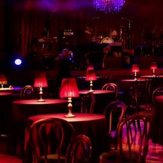 tables and chairs with red lamps on them in a dark lit room, set up for an event