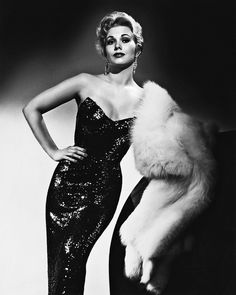 an old photo of a woman in a black dress and fur stole with her hands on her hips