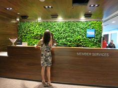 a woman standing in front of a wooden reception desk with green wall behind it and people sitting at the counter