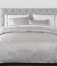 a white bed with silver sheets and pillows