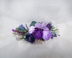 purple flowers and greenery sit on top of a hair comb in front of a white background