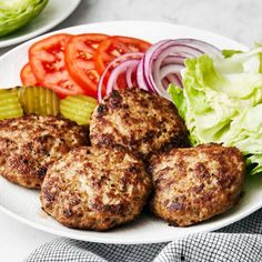 three hamburger patties on a plate with lettuce, tomato and pickles