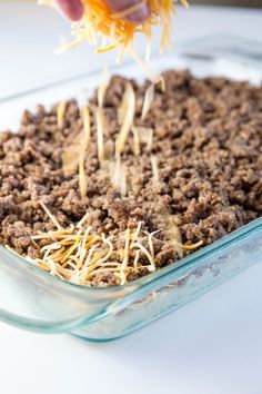 someone sprinkling cheese on top of a casserole in a glass dish