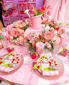 the table is set with pink flowers and plates, cups, and utensils