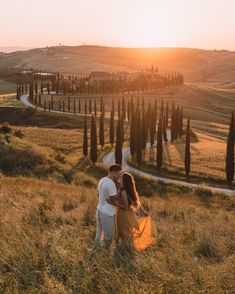 a man and woman standing on top of a lush green hillside next to an olive grove