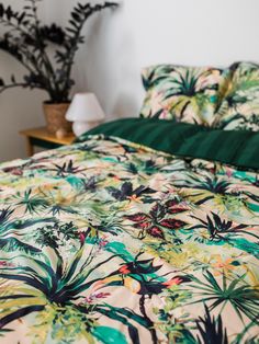 a bed with green and yellow comforter next to a plant in a vase on the nightstand