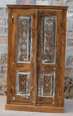 an old wooden armoire with carvings on the front and side panels, sitting against a brick wall