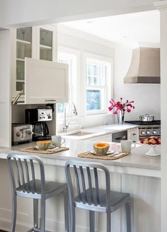 two chairs are sitting at the bar in this white kitchen with stainless steel appliances and counter tops