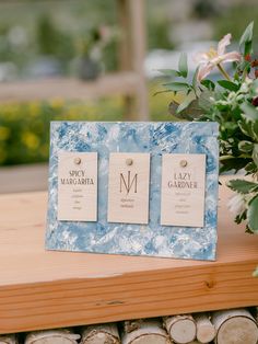 two wooden signs sitting on top of a table next to flowers and wood slices in front of them