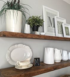 two wooden shelves filled with white dishes and vases on top of each other next to framed pictures