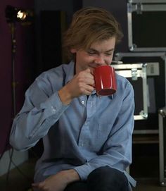 a woman sitting on the floor drinking from a red coffee mug in front of her