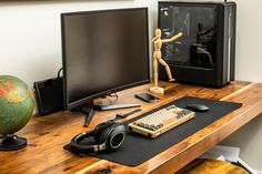 a wooden desk topped with a computer monitor next to a keyboard and headphones on top of it