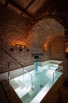 an indoor swimming pool surrounded by brick walls and stone steps leading up to the ceiling