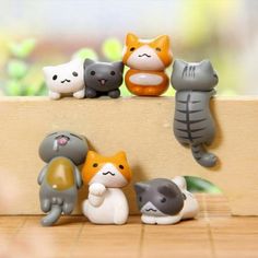 small toy figurines of cats and kittens sitting on a wooden surface with plants in the background