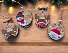 three christmas ornament hanging on a wooden table next to a tree with lights