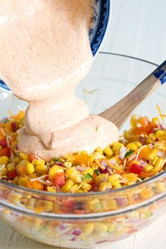 a bowl filled with corn and dressing next to a wooden spoon