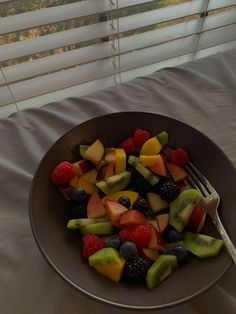 a bowl filled with fruit sitting on top of a bed next to a white window