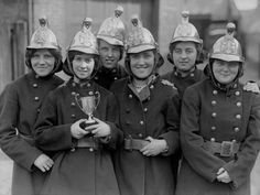 black and white photograph of women in uniforms with hats on their heads holding a trophy