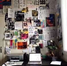 a laptop computer sitting on top of a desk next to a wall covered in pictures